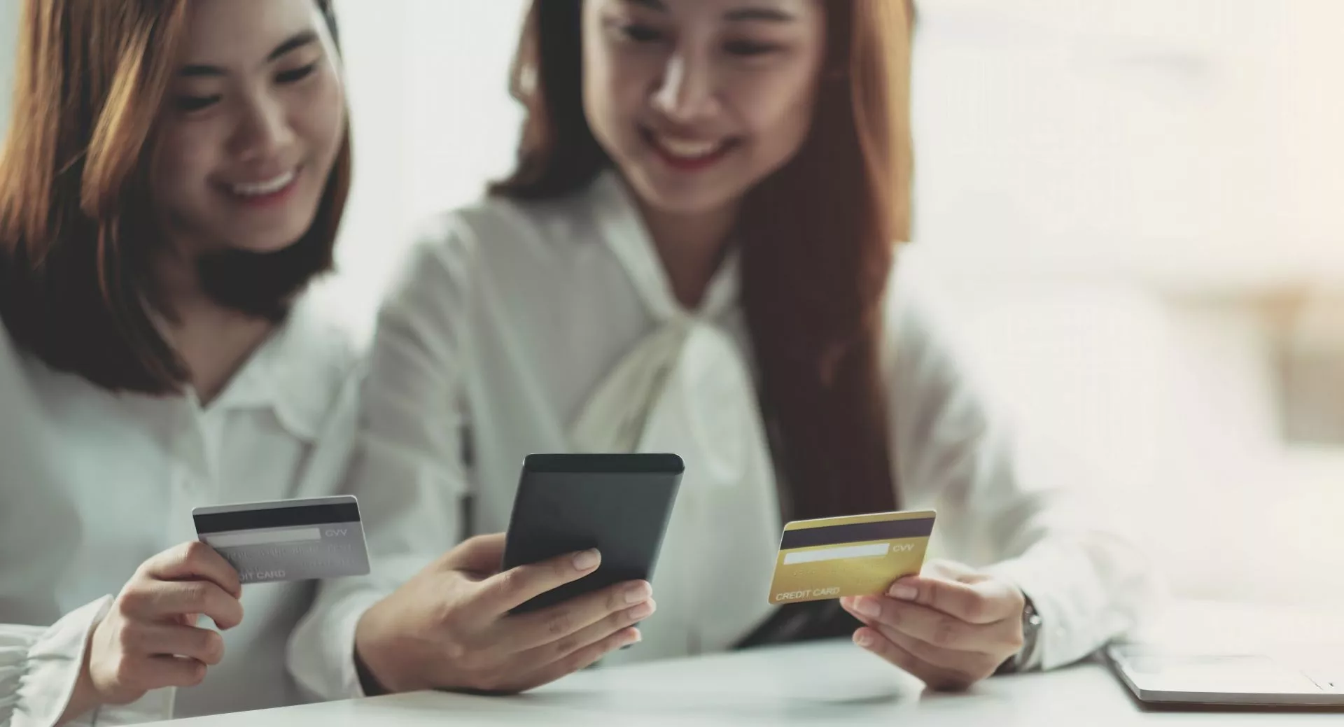 202604151035.webp 兩名女性坐在桌前使用手機與信用卡進行線上交易,畫面呈現信用卡支付與數位金融操作情境,適合用於信用卡換現金、線上刷卡與金融服務主題配圖